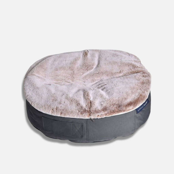 En rund, plysset hundeseng fra Ambient Lounge med en blød, lys beige imiteret pels på toppen og en mørkegrå bund - denne stilfulde hundeseng cappuccino vises på en almindelig lys baggrund.