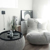Et lyst, minimalistisk rum med en hyggelig grå salongstol, et rundt sort sofabord med en vase og et stearinlys, en slangeplante og indrammet kunst og en stor kalender, der står op ad væggen på trægulvet.