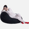 En person i lyst loungewear og røde sokker slapper af på en sort Ambient Lounge-sækkestol og lytter til musik med hovedtelefoner på en almindelig hvid baggrund.