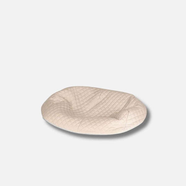En beige, oval allergivennlig hundeseng med quiltet toptræk, med en let fordybet overflade, vist på en almindelig hvid baggrund.