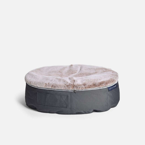 En rund, grå hundeseng fra Ambient Lounge med blød, lysebrun kunstpels på toppen, der giver optimal komfort for hund, står på en almindelig hvid baggrund.