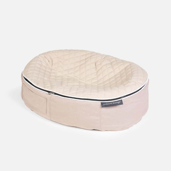 En beige, quiltet oval hundeseng med en blød ThermoQuilt-polstret overflade og en lav, stofbeklædt side. På forsiden sidder et lille mærke med teksten Ambient Lounge. Baggrunden er helt hvid.
