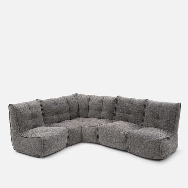 En moderne, L-formet Ambient Lounge Mod 4 L-sofa med blødt, tuftet, gråt stofbetræk tilbyder fleksible møbler med flere forbundne sæde- og ryglænssektioner, der står på en almindelig hvid baggrund.