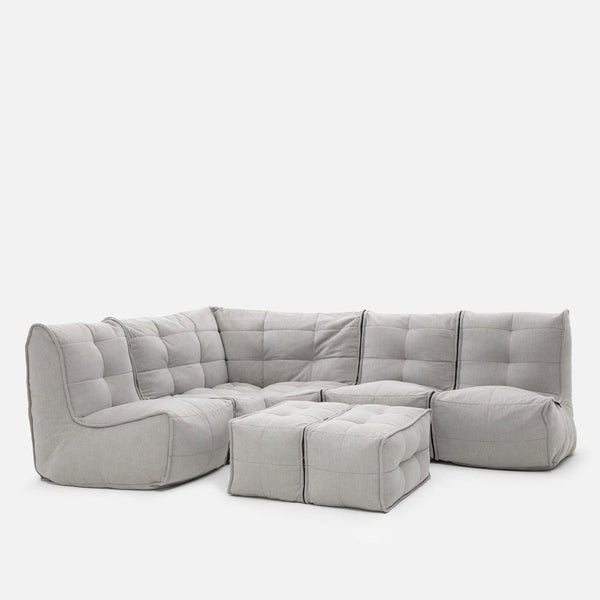 En moderne, modulopbygget lysegrå Modulsofa med to matchende ottomaner, med blødt, tuftet betræk og plys, boxy puder - perfekt til hjemmekino-møbler - arrangeret i en L-form mod en ensfarvet hvid baggrund.
