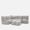 En moderne, modulopbygget lysegrå Modulsofa med to matchende ottomaner, med blødt, tuftet betræk og plys, boxy puder - perfekt til hjemmekino-møbler - arrangeret i en L-form mod en ensfarvet hvid baggrund.