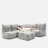 En kvinde i en hvid kjole ligger på en lysegrå, tuftet Modulsofa med matchende ottoman og hviler hovedet på en pude i en afslappet stilling. Det alsidige design blander komfort og stil, perfekt til moderne rum. Baggrunden er almindelig hvid.