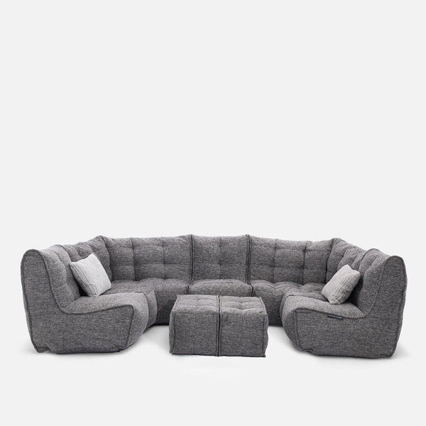 En moderne grå modulær sofa med tuftede puder, to matchende ottomaner og to accentpuder, arrangeret i en U-form mod en almindelig hvid baggrund - en perfekt moderne stueløsning fra Ambient Lounge.