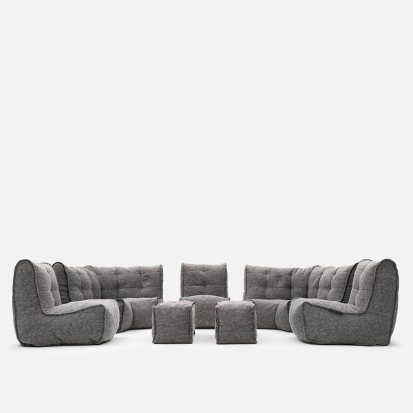A modulær sofa fra Ambient Lounge, denne moderne stueløsning har tuftede puder og består af to hjørnedeler, to armløse dele og fire puffer, arrangeret i en U-form på hvid baggrund.
