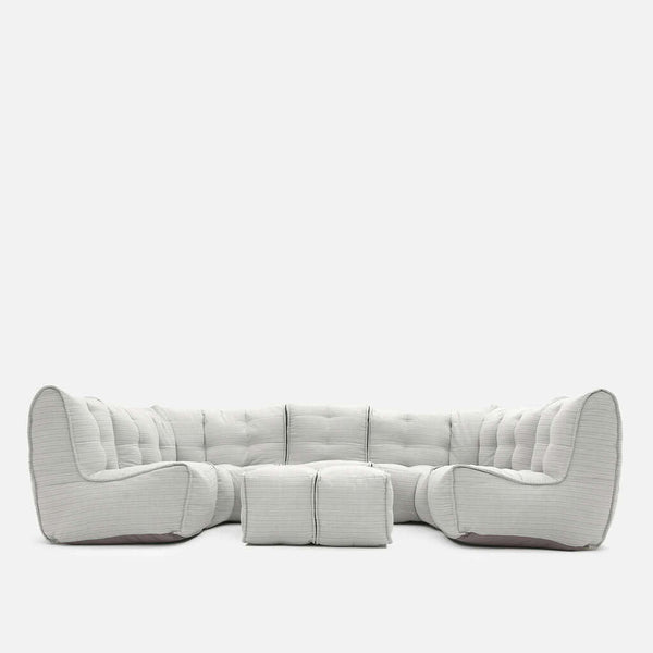 En moderne, lysegrå Ambient Lounge sektionssofa med dybe puder og to matchende firkantede ottomaner, der alle er arrangeret i en L-form mod en almindelig hvid baggrund, perfekt til at skabe en hyggelig loungesofa-stemning.
