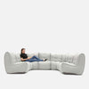 En person sidder afslappet med strakte ben i en stor, moderne Ambient Lounge-sædesofa med tuftede puder på en almindelig hvid baggrund.