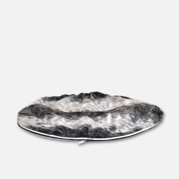 En rund, flad hundeseng med en fluffy, sort, hvid og grå fuskepelstrekk og luksuriøs pelstopp, vist mod en almindelig lysegrå baggrund.
