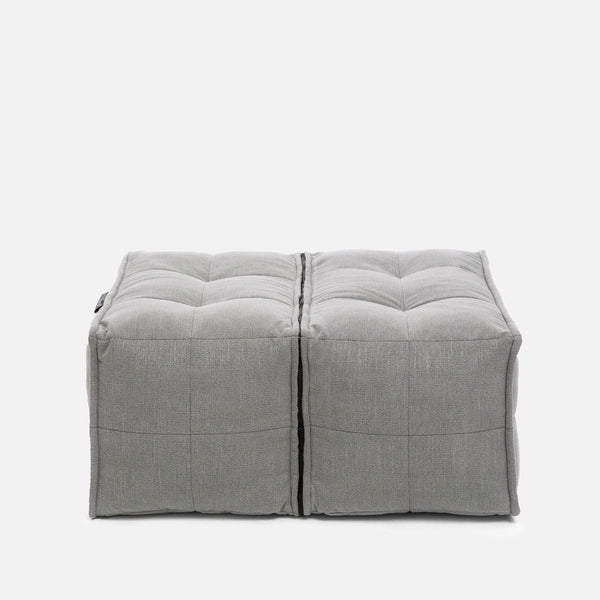 To grå, firkantede Twin Ottomans fra Ambient Lounge har tuftede detaljer og synlige sømme, arrangeret side om side på en almindelig hvid baggrund for et moderne designer-ottoman-look.
