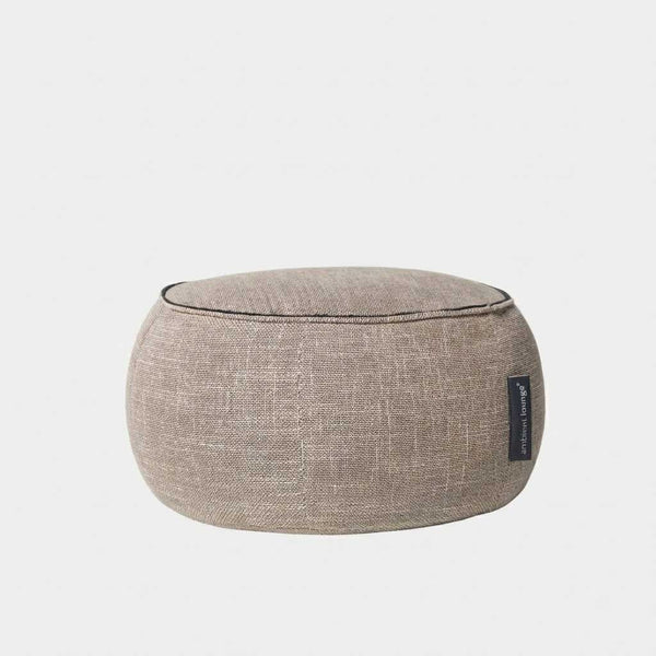 En rund, lysebrun stofpuf eller gulvpude med synlige syninger og et lille sort mærkat på siden. Dette alsidige stykke passer perfekt til en Butterfly-sofa eller fungerer som en stilfuld Wing Ottoman på en almindelig hvid baggrund.