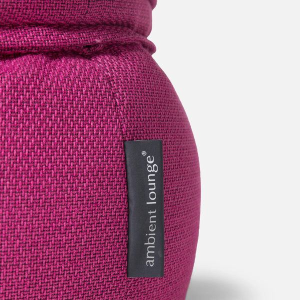 Nærbillede af en sækkestol i magentafarvet stof med en sort, lodret etiket med teksten ambient lounge® syet på siden. Den er designet til komfort og har en pude af memory-skum. Baggrunden er ensfarvet og lys.