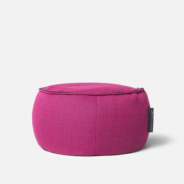 En rund, magenta puf med struktureret stof og et lille sort mærke på siden, udformet som en elegant Wing Ottoman, på en almindelig hvid baggrund.