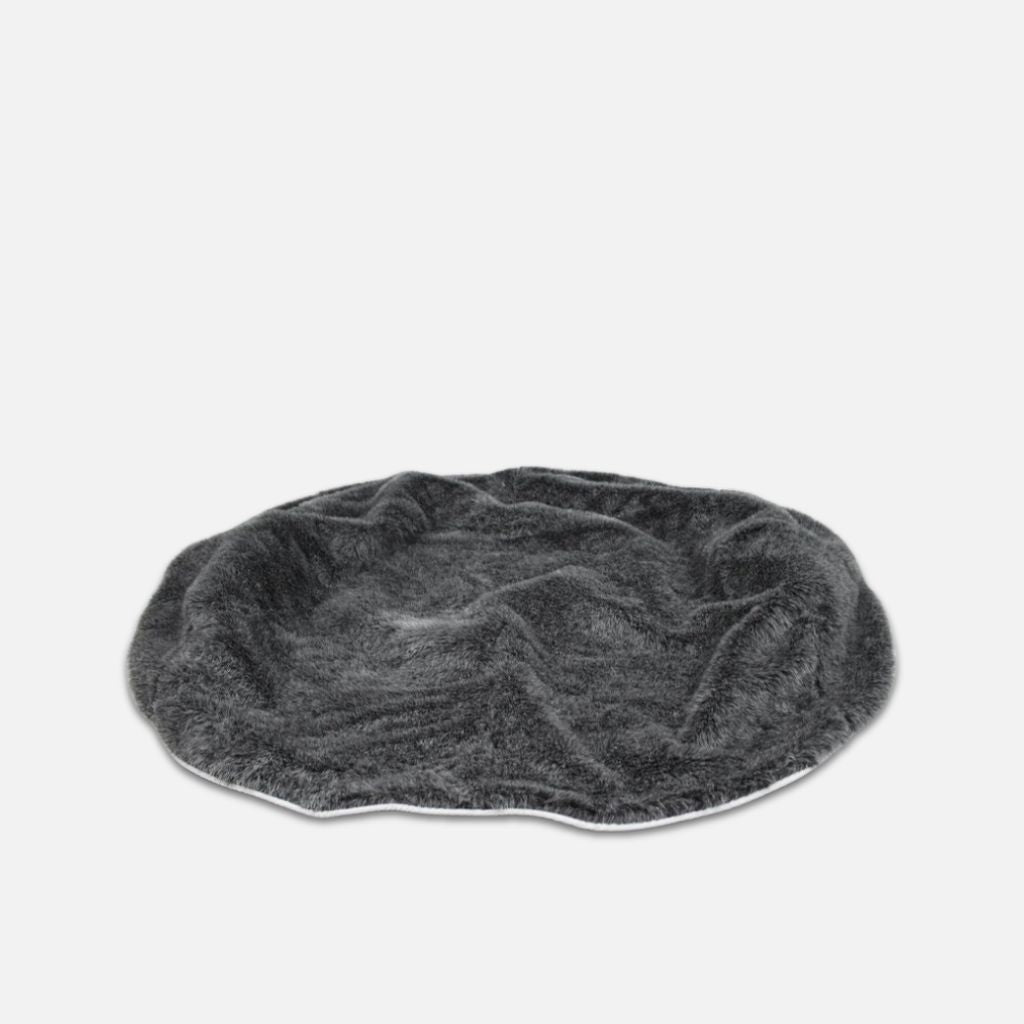 En rund, mørkegrå, plysset kæledyrsseng med en blød, lodden tekstur er vist på en almindelig hvid baggrund. Denne Ambient Lounge fuskepelstrekk hundeseng ser lidt krøllet ud og har ingen hævede kanter.